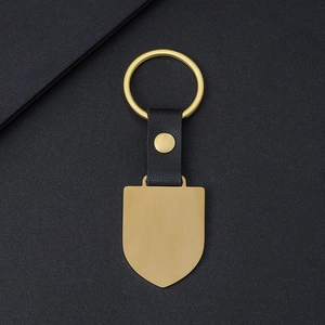 Custom gold shield metal keychain with black leather strap on a textured dark background