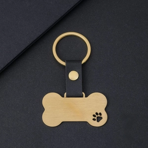 Golden bone-shaped pet tag with hollow paw print and black leather keychain strap