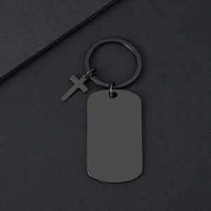 Primer plano del llavero con placa militar negra mate y colgante de cruz sobre fondo oscuro