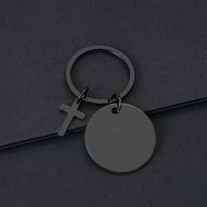 Detalle de llavero de metal negro mate con disco redondo y colgante de cruz para grabar