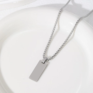 Dettaglio di un ciondolo rettangolare argento con catena a scatola su ceramica bianca