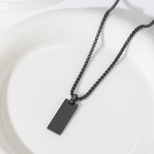 Dettaglio del pendente rettangolare nero con catena box abbinata su ceramica bianca