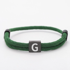 Detail of dark green braided cord bracelet with matte black metal square letter G charm
