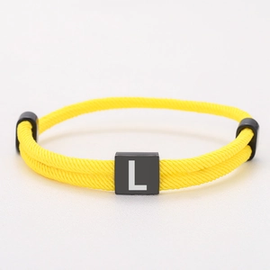 Detail of yellow woven Milan rope bracelet with a black square block featuring letter L