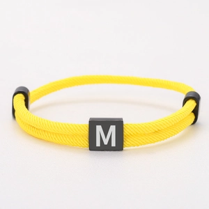 Detailed close-up of yellow braided Milan rope bracelet with black letter M square charm