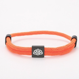 Detailed close-up of orange braided rope bracelet with black lotus engraved charm
