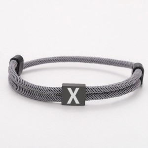 Detail of dark grey braided cord bracelet featuring a black metal square with letter X