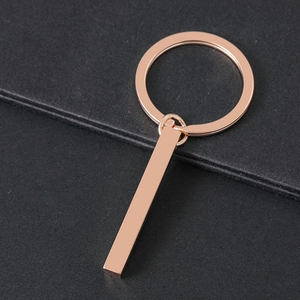 Polished rose gold minimalist stainless steel cube keychain on a textured dark background