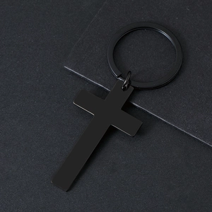 Close-up of a matte black stainless steel cross keychain on a textured dark background