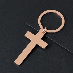 Polished rose gold stainless steel cross keychain on a textured dark background