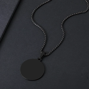 Vista macro di un ciondolo rotondo minimalista in acciaio nero su catena a maglia quadra