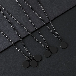 Primer plano de collares de acero inoxidable negro con colgantes redondos sobre fondo gris