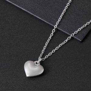 Macro detail of a silver heart pendant with matte finish on a black textured background