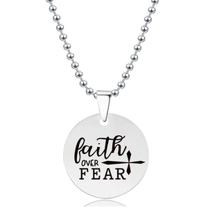 Macrodetail van de ronde roestvrijstalen hanger met faith OVER FEAR gravure en kruisicoon