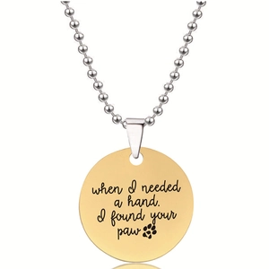 Detail van gouden ronde hanger met gegraveerde tekst en zilverkleurige bolletjesketting