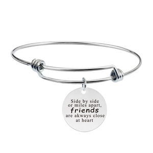 Detail of adjustable stainless steel bangle with engraved friendship quote on round charm