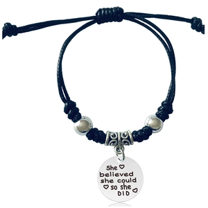 Close-up of woven bracelet with polished charm engraved She believed she could so she did