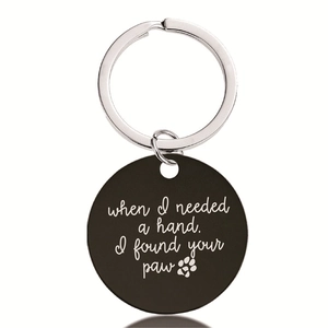 Close-up of black metal keychain with engraved pet paw print and sentimental message