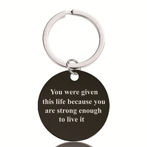 Macro detail of black stainless steel round keychain with engraved motivational quote