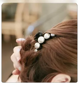 Détail d'une pince à cheveux noire avec perles blanches sur des cheveux bruns ondulés