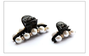 Dettaglio di fermagli per capelli con perle e strass in resina nera e accenti dorati