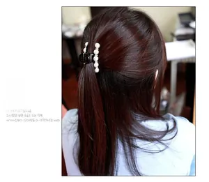 Dettaglio di una molletta nera con perle bianche indossata su capelli semiraccolti
