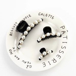 Set di tre mollette per capelli nere con perle e strass su un piatto bianco