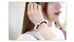 Détail des perles roses sur l'élastique à cheveux noir porté au poignet féminin