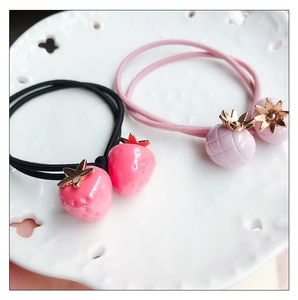 Détail de breloques fraises sur des élastiques à cheveux dans un plat en porcelaine