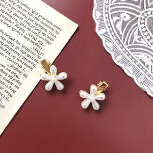 Detail of two gold flower hair clips with white pearls on a deep red background