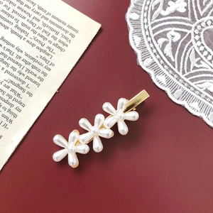 Detail of elegant gold hairpin with three white pearl flowers on deep red background