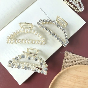 Detailed view of three luxury gold alloy hair claws with pearls and rhinestones on a book