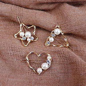 Dettaglio di fermagli per capelli dorati a forma di stella, cuore e triangolo con perle