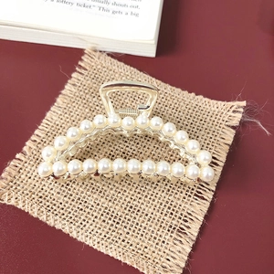 Detail shot of a golden claw clip featuring elegant pearls and rhinestones on burlap