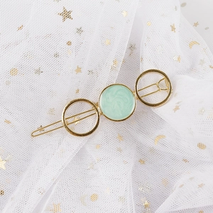 Detail of a gold metal hair clip featuring a mint green marble enamel circular inlay design