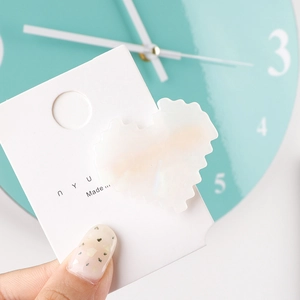 Macro shot of a cream-white heart-shaped acetate hair clip with pixelated edges on card