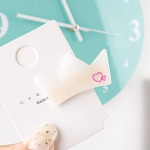 Macro shot of a cream-colored crown hair clip with a pink heart detail on a card