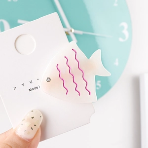 Close-up of a fish-shaped acetate hair clip with pink wavy patterns and crystal eye detail