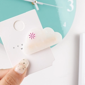 Detailed view of a white cloud hair clip with pink sun accent on a display card