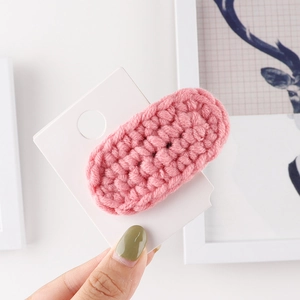 Handmade pink crochet wool BB hair clip shown on card and held by hand for scale