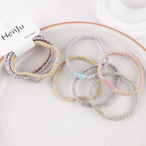 Detail of braided macaron elastic hair bands on a beige ceramic plate with brand tag