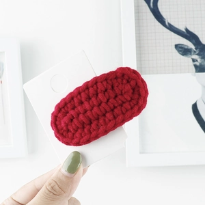 Detail of red hand-knitted yarn BB hair clip showing the thick wool texture and stitching
