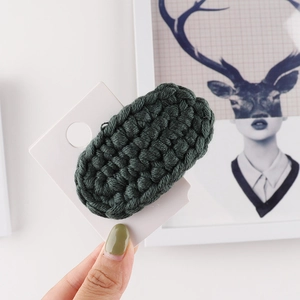 Close-up of hand-knitted dark green wool hair clip with detailed crochet texture on card