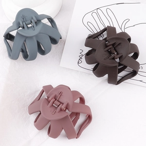 Close-up of three matte hair claws in grey-blue, dark brown, and dusty pink colors