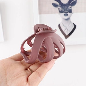 Close-up of matte dusky rose hair claw clip held by hand in a minimalist setting