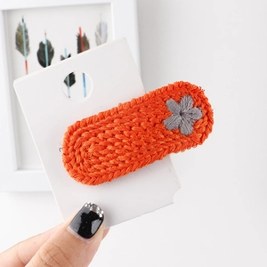 Detail einer handgestrickten orangefarbenen Haarspange mit grauer Blumenstickerei