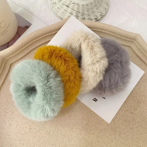 Close-up of four plush faux rabbit fur scrunchies in mint green, yellow, grey, and cream