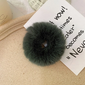 Detailed view of a plush dark green faux rabbit fur scrunchie on a beige tray