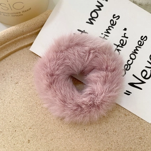 Detailed shot of soft pink faux rabbit fur scrunchie on a minimalist beige desktop