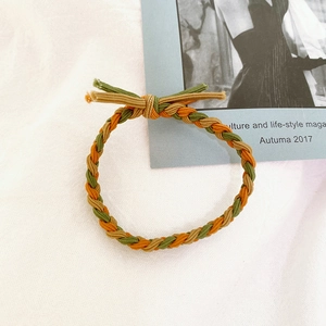 Detail view of a braided elastic hair tie featuring green, brown, and orange interwoven cords
